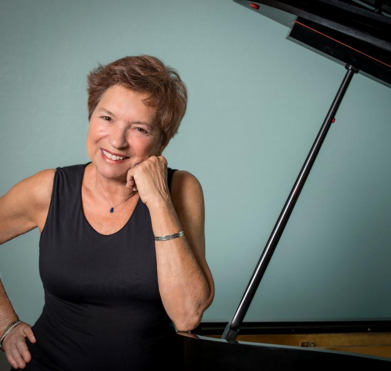 Peggy Stern standing next to her piano.